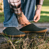 Person adjusting their jeans with green slippers outdoors
