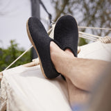 Person wearing black slippers relaxing in a hammock with blurred greenery in the background