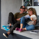 Two people sitting on a couch, one reading a book, in a casual setting.