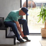 Man sitting on a step tying his shoe indoors with a plant in the background