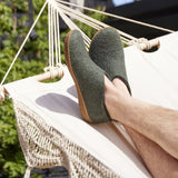 Person wearing forest green slippers with honey rubber soles on a hammock outdoors.