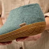 Close-up of a north sea slipper with honey rubber sole held by a person wearing a beige shirt.