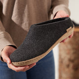 Person holding a dark gray slipper with leather sole