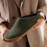 Green slipper with rubber sole held by a person wearing a beige coat.