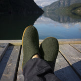Feet wearing green shoes on a wooden deck with a mountain and lake view.