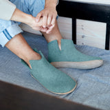 Person wearing teal slippers sitting on a couch.