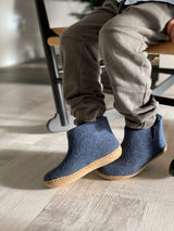 Child sitting down wearing denim wool boots with a beige leather sole.