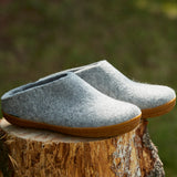 Pair of gray slippers with brown soles on a wooden stump with a blurred natural background