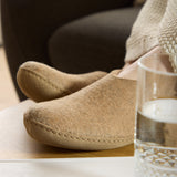 Sand slippers on a wooden surface with a glass of water in the foreground.