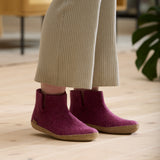 Cranberry ankle boots worn indoors on a wooden floor.