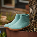 Pair of teal boots with honey rubber soles in a pot with plants
