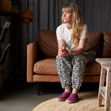 Woman sitting on a brown couch wearing a white shirt and zebra print pants, with a neutral background.
