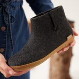 Person holding a dark gray boot with a honey rubber sole