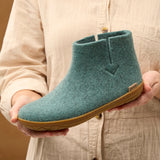 Person holding a teal ankle boot with a honey rubber sole