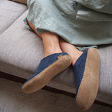 Person wearing denim and leather sole slippers sitting on a couch.