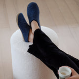 Person wearing denim slippers and holding a white mug on a light wooden floor.