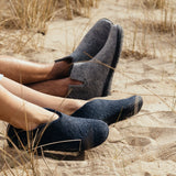 Two pairs of feet wearing gray and navy shoes on a sandy surface with grass.