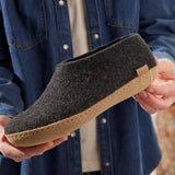 Person holding a dark gray slipper with a brown sole