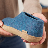 Blue slipper with beige sole held by a person, brand 'plae' visible