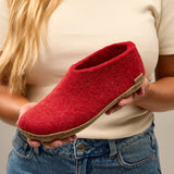 Red slipper held by a person wearing a beige shirt and blue jeans.