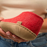 Red and beige slippers held by a person with a blurred background