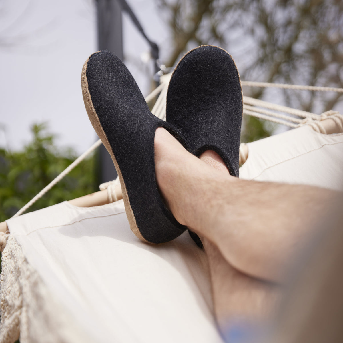 Person wearing black slippers relaxing in a hammock with blurred greenery in the background