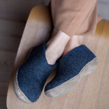 Person wearing blue slip-on shoes with beige soles on a wooden floor.