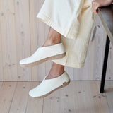 White slippers worn with light-colored pants on a wooden floor.