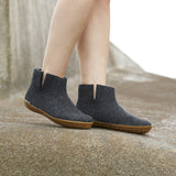 Dark Gray ankle boots with  honey rubber soles worn by a person on a stone surface.