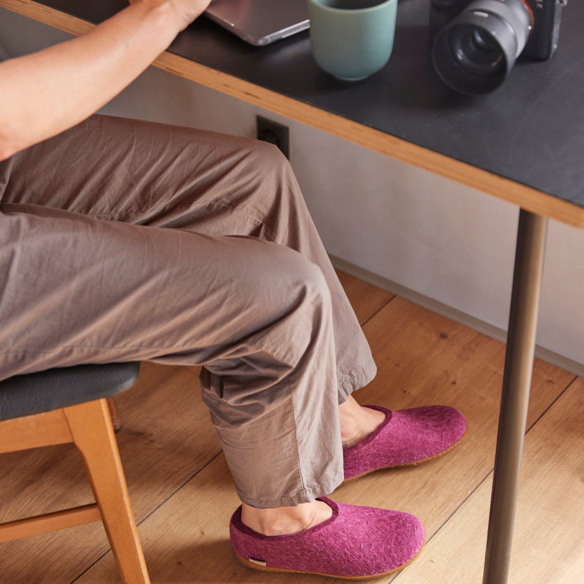 Person sitting at a desk wearing cranberry slippers on a wooden floor.