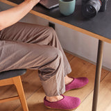 Person sitting at a desk wearing cranberry slippers on a wooden floor.