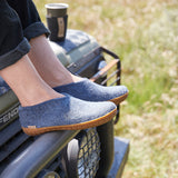 Person wearing blue shoes with honey rubber soles sitting on a vehicle in a grassy area