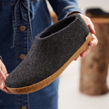 Person holding a dark gray slipper with a honey rubber sole against a blurred background