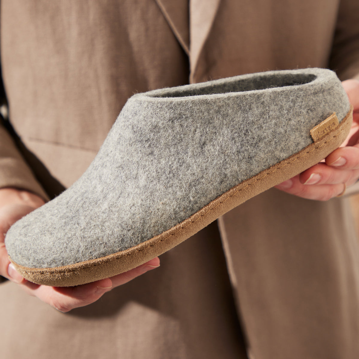 Person holding a gray slipper with a leather sole
