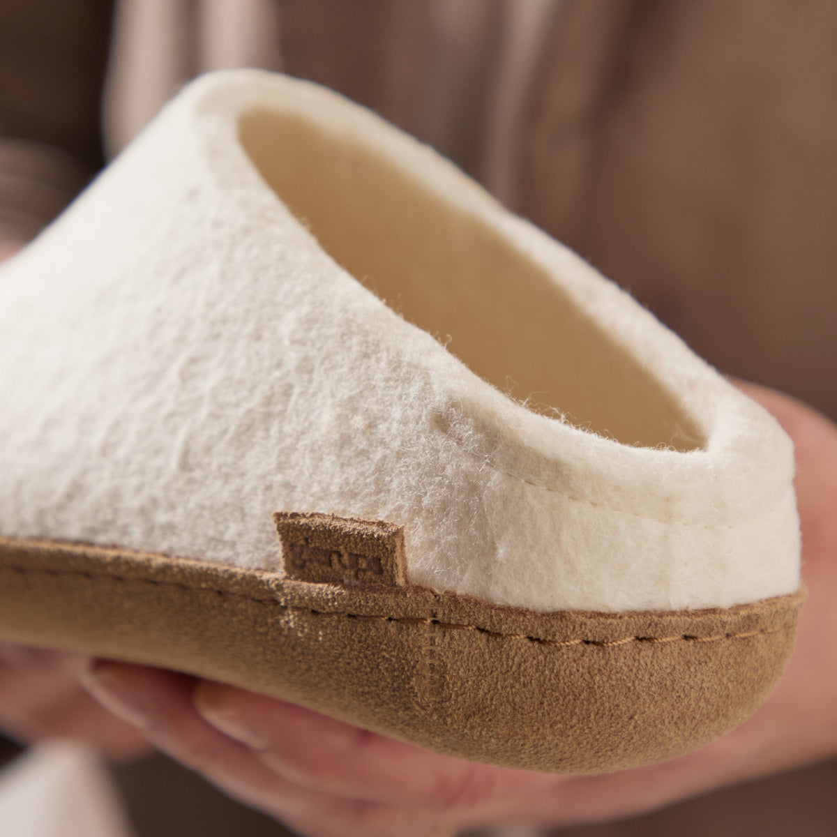 Close-up of a white slipper with leather sole held by a hand