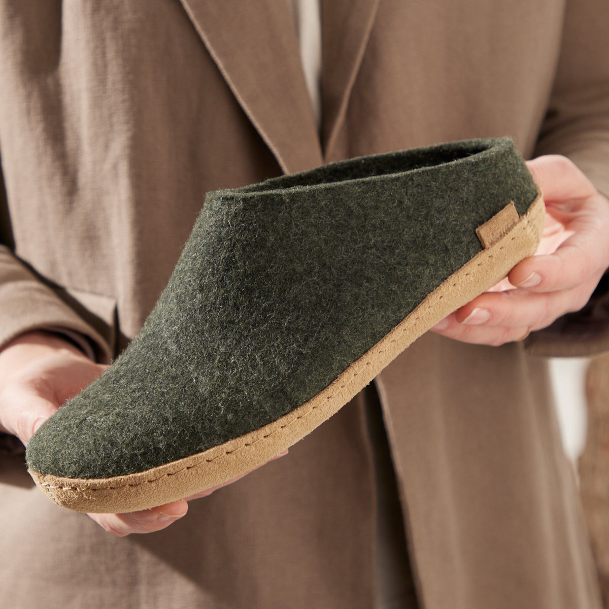 Green felt shoe held by a person wearing a brown coat