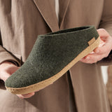 Green felt shoe held by a person wearing a brown coat