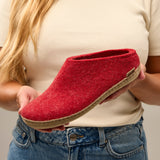 Red slipper held by a person wearing a beige shirt and blue jeans.