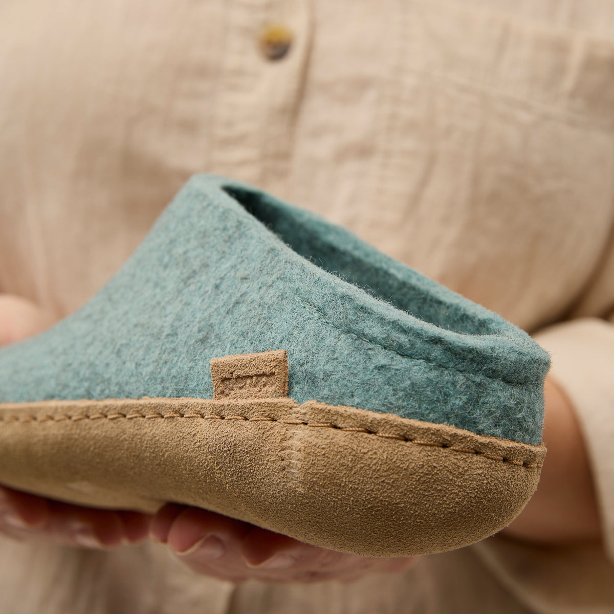 Close-up of a north sea slipper with a leather sole held by a person wearing a beige shirt.