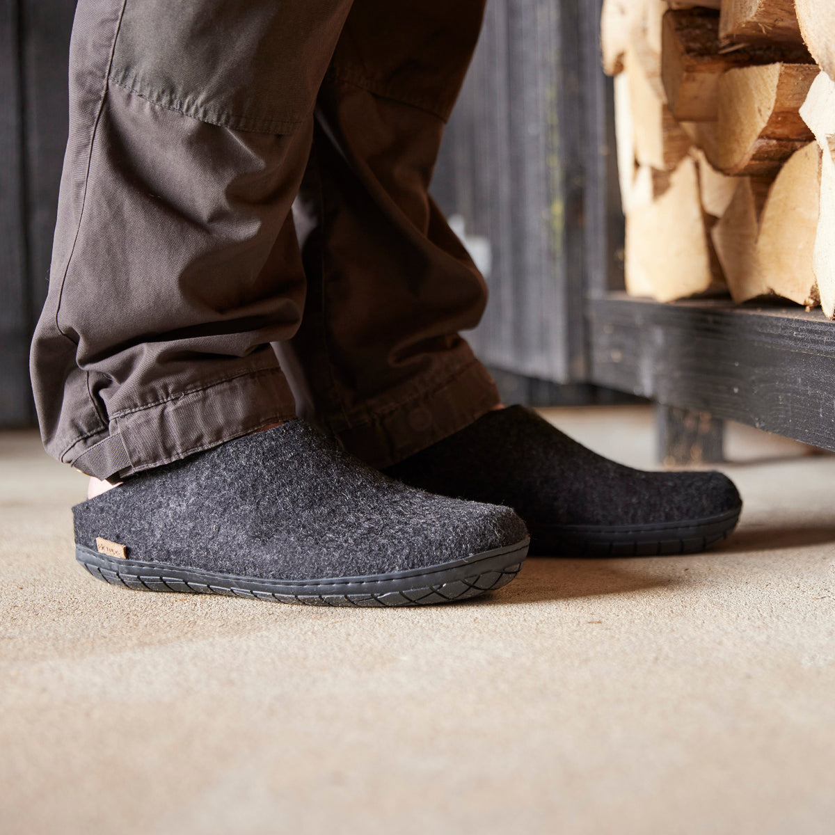 Person wearing gray and black slippers indoors with a wooden shelf in the background.