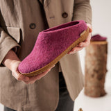 Person holding a cranberry wool slipper with a rubber sole indoors