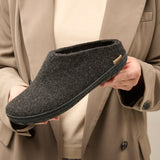 Person holding a dark gray slipper with a beige coat background