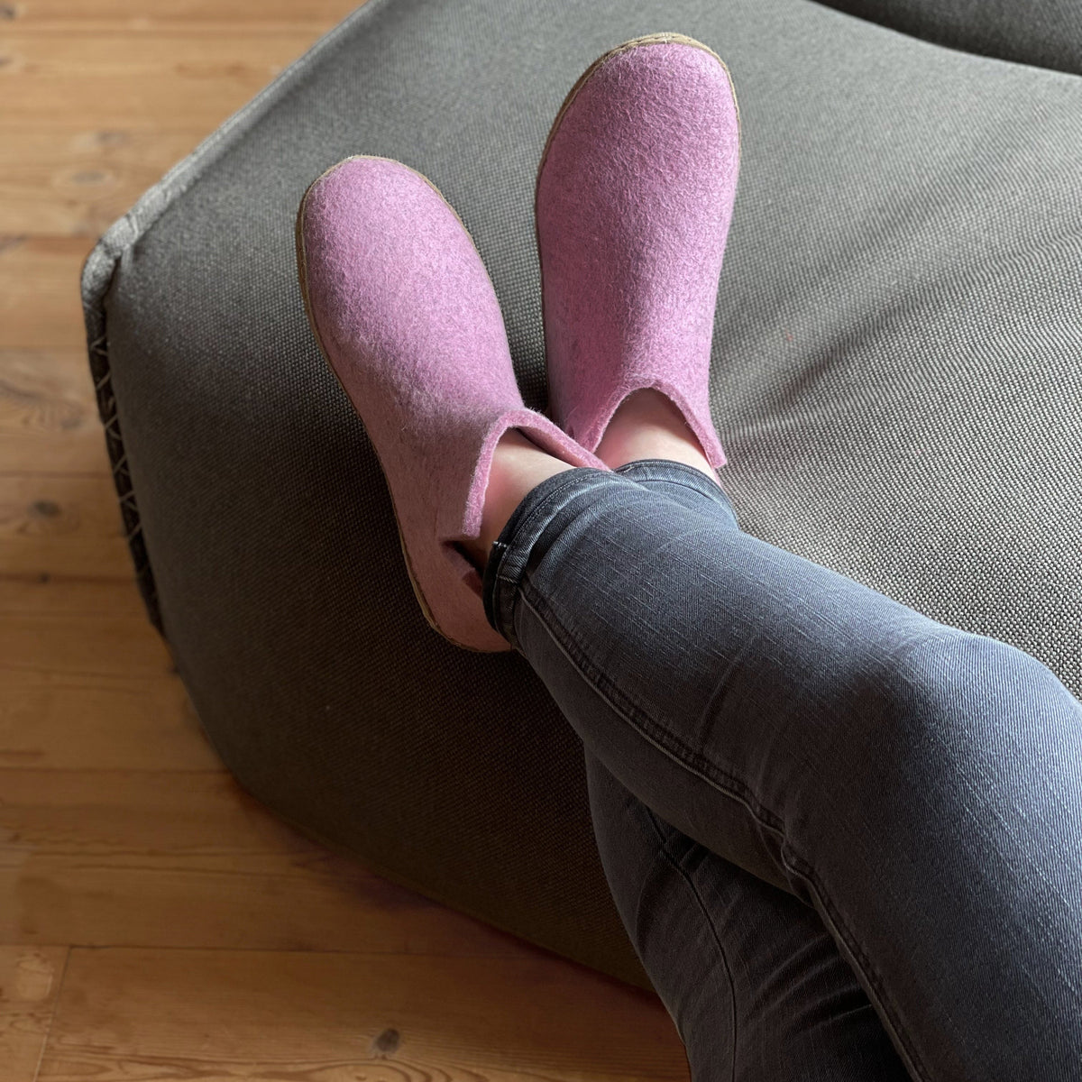 Person wearing pink slippers on a gray cushioned chair with wooden floor.