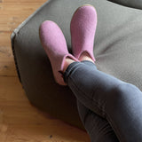 Person wearing pink slippers on a gray cushioned chair with wooden floor.
