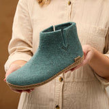 Person holding a teal ankle boot with a beige background