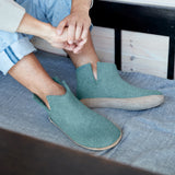 Person wearing teal slippers sitting on a couch.