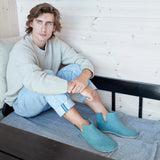 Person wearing blue slip-on shoes sitting on a couch.