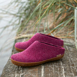 Pair of cranberry slippers with rubber soles on a wooden surface with grass in the background