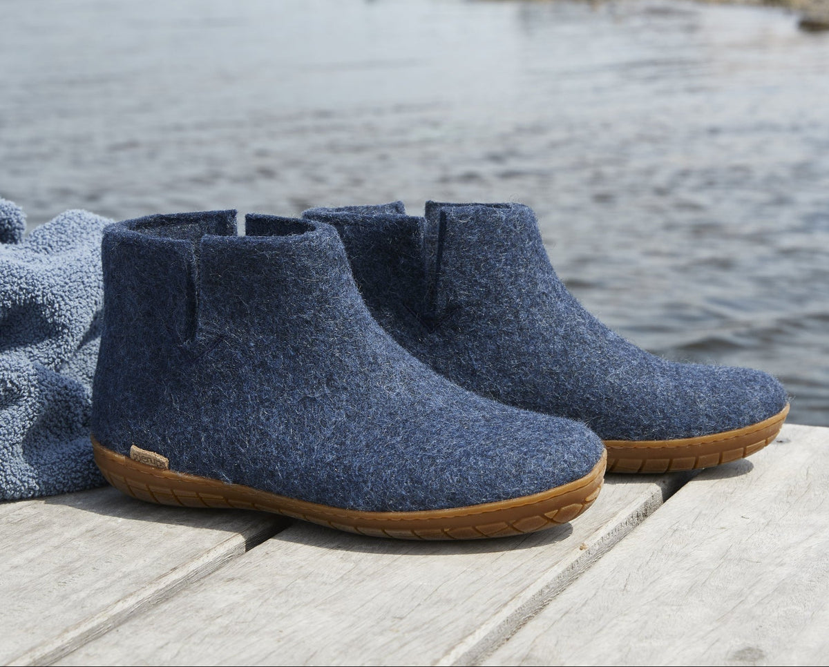 Pair of blue ankle boots with honey rubber  soles on a wooden dock by a body of water.
