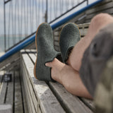 Person wearing green ankle boots with  honey rubber, sitting on a wooden bench.